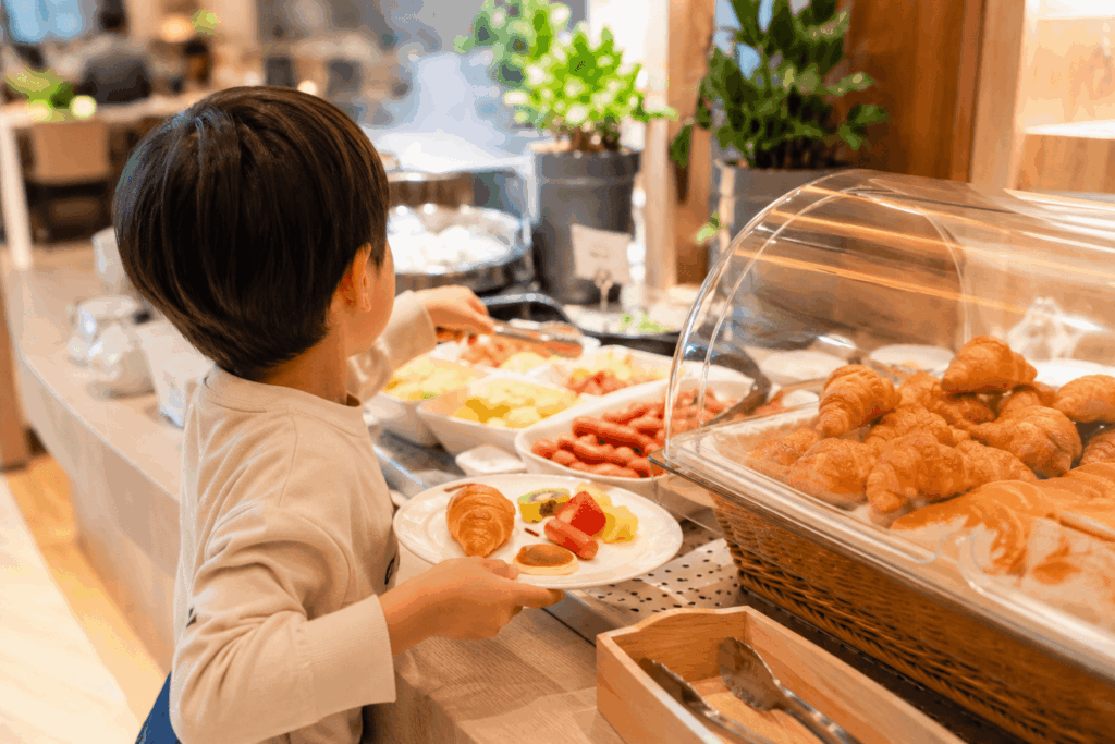 キッズビュッフェ台で子供が好きなパンや果物を選ぶ後ろ姿