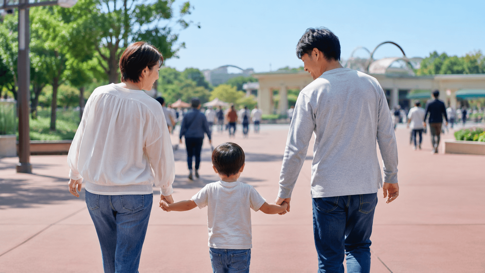 小さな子どもと手をつないでテーマパークを歩く家族のイメージ