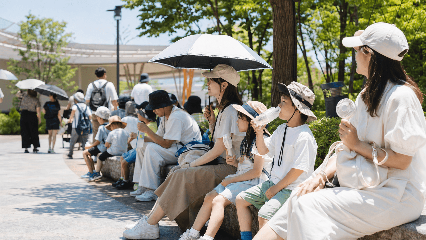 夏の屋外テーマパークで暑さ対策をする来園者のイメージ