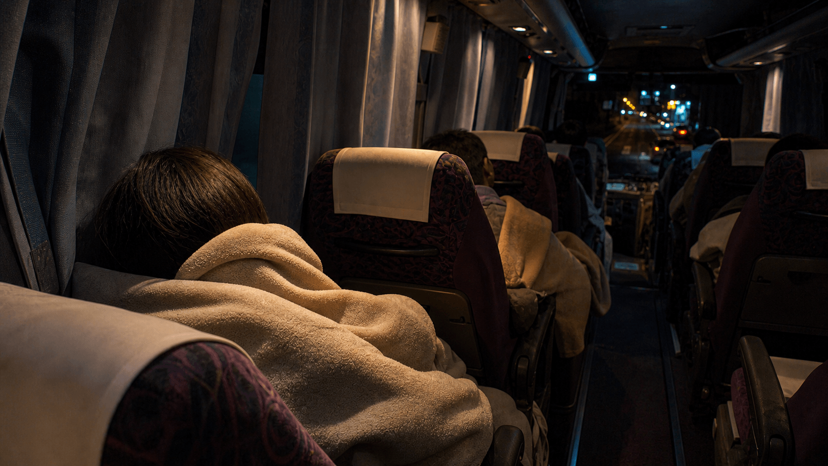 夜行バスの車内で毛布にくるまり眠る乗客の後ろ姿