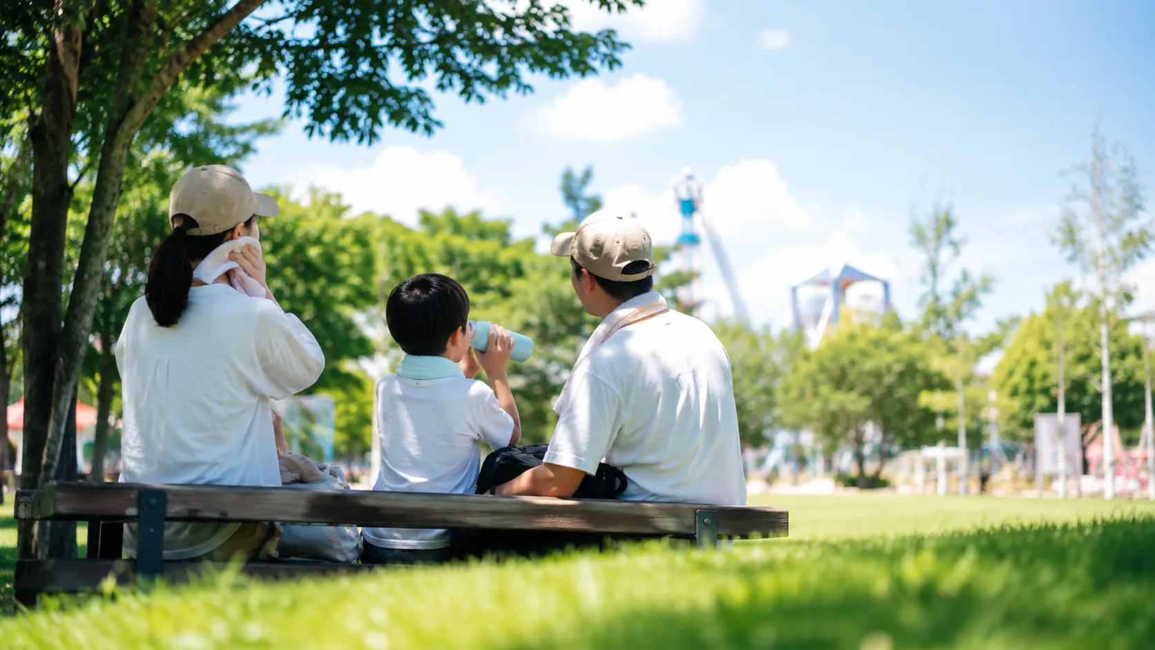 夏の屋外テーマパークで、水分補給と休憩を意識して過ごす来園者のイメージ