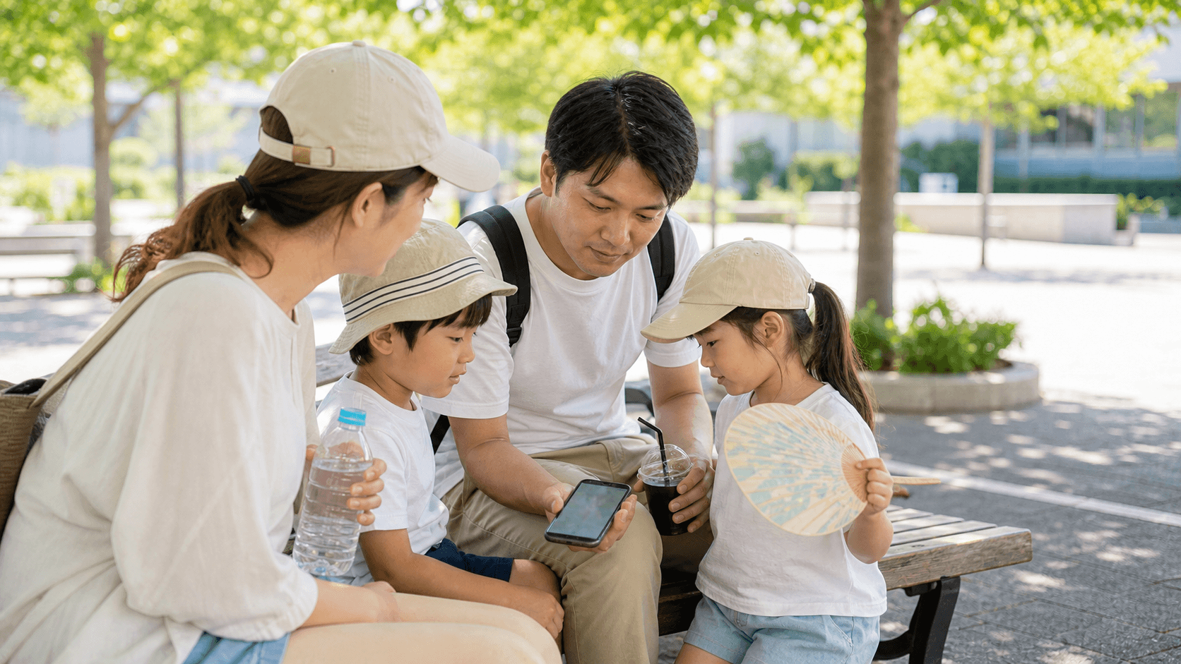 日陰のベンチでスマートフォンの地図を確認しながら休憩する家族
