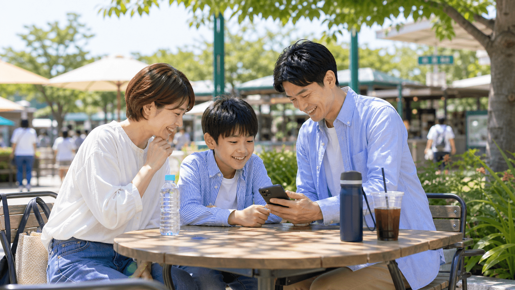 木陰のテラス席でスマートフォンを見ながら休憩する親子
