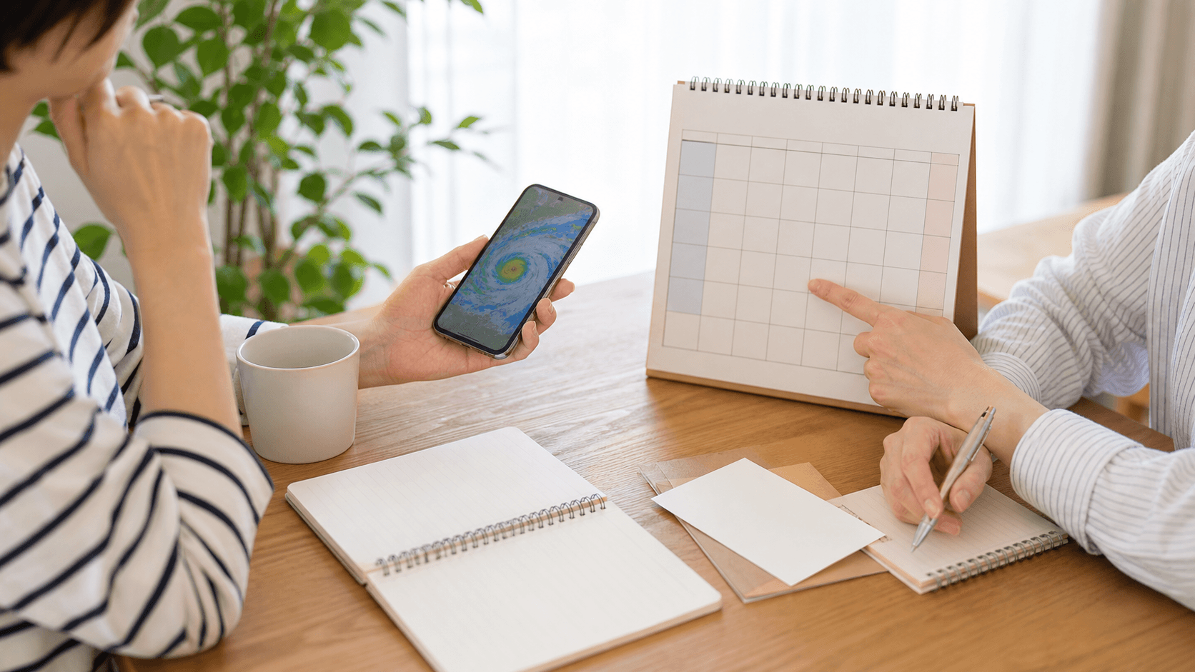 スマートフォンの気象情報を見ながら、カレンダーで予定の変更を相談する2人