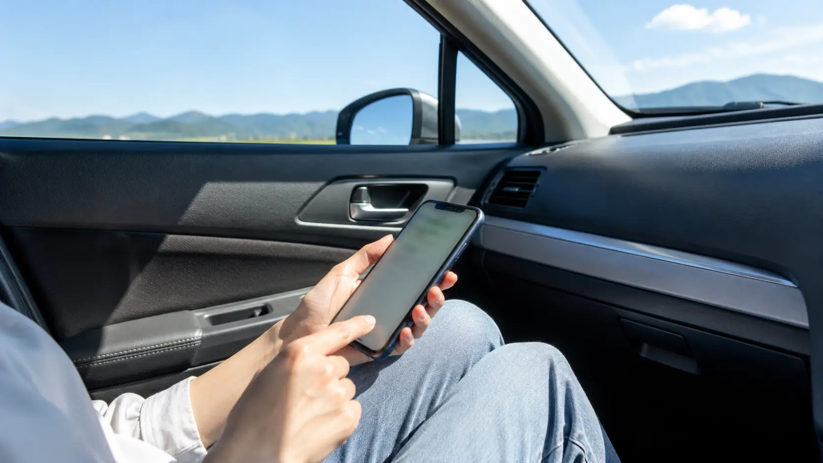 朝の駐車場に立ちスマートフォンで運行状況を確かめている人の後ろ姿