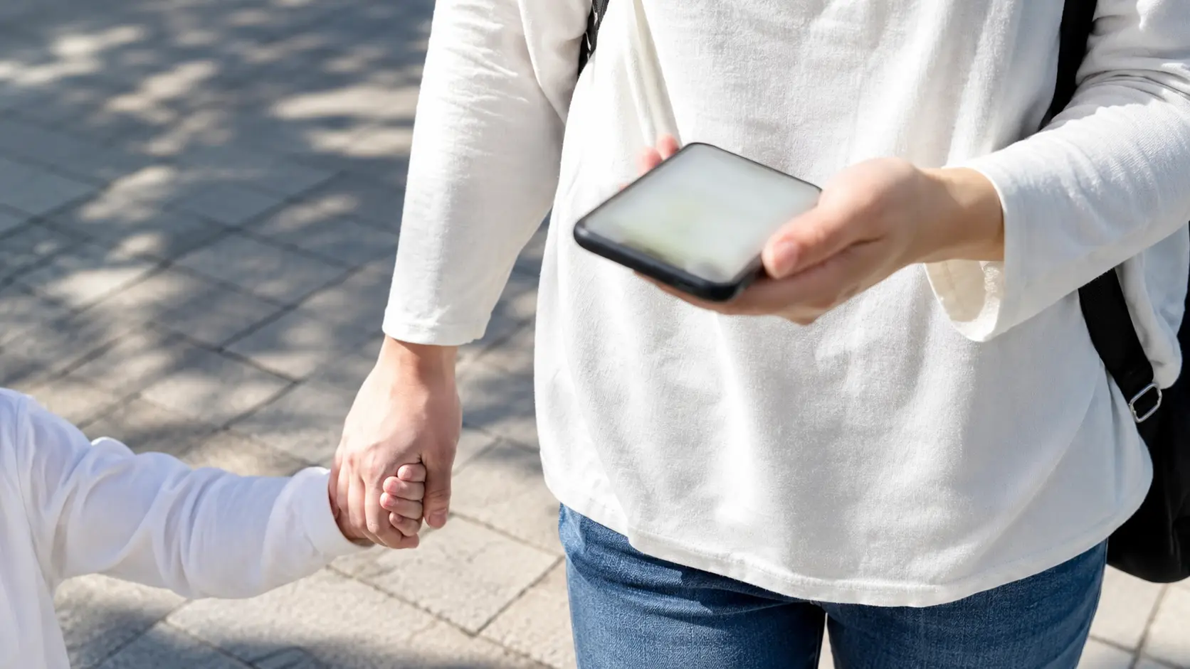 子どもの手を引きながら片手でスマートフォンを見ている大人の手元