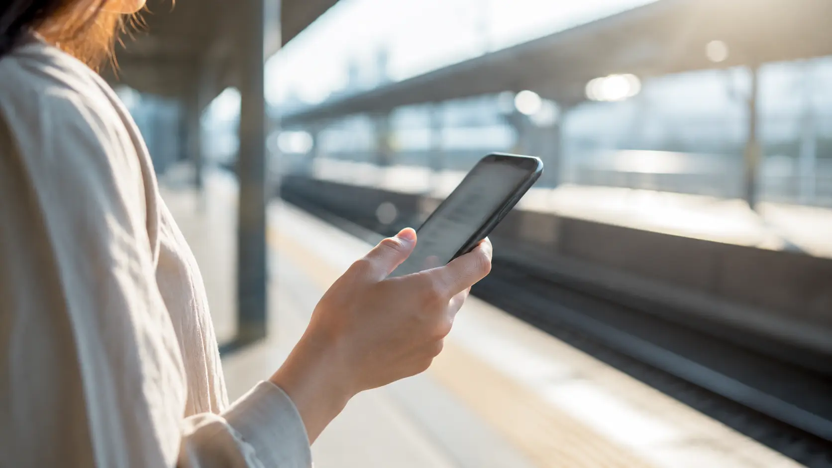 駅のホームでスマートフォンの画面を確認している手元