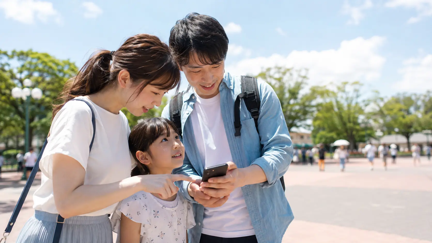 広場でスマートフォンの画面を一緒にのぞき込む親子