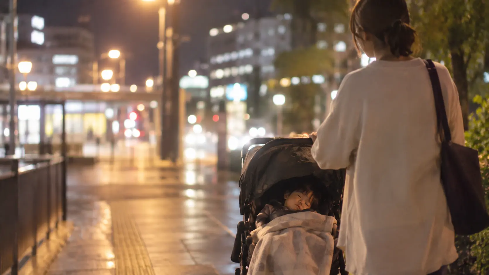 夜の帰り道でベビーカーに乗ったまま眠ってしまった子どもと保護者
